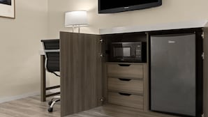 A compact kitchenette with a microwave, a refrigerator, a chair, and a wall-mounted TV. - The Dylan, a Baymont by Wyndham (Seattle)
