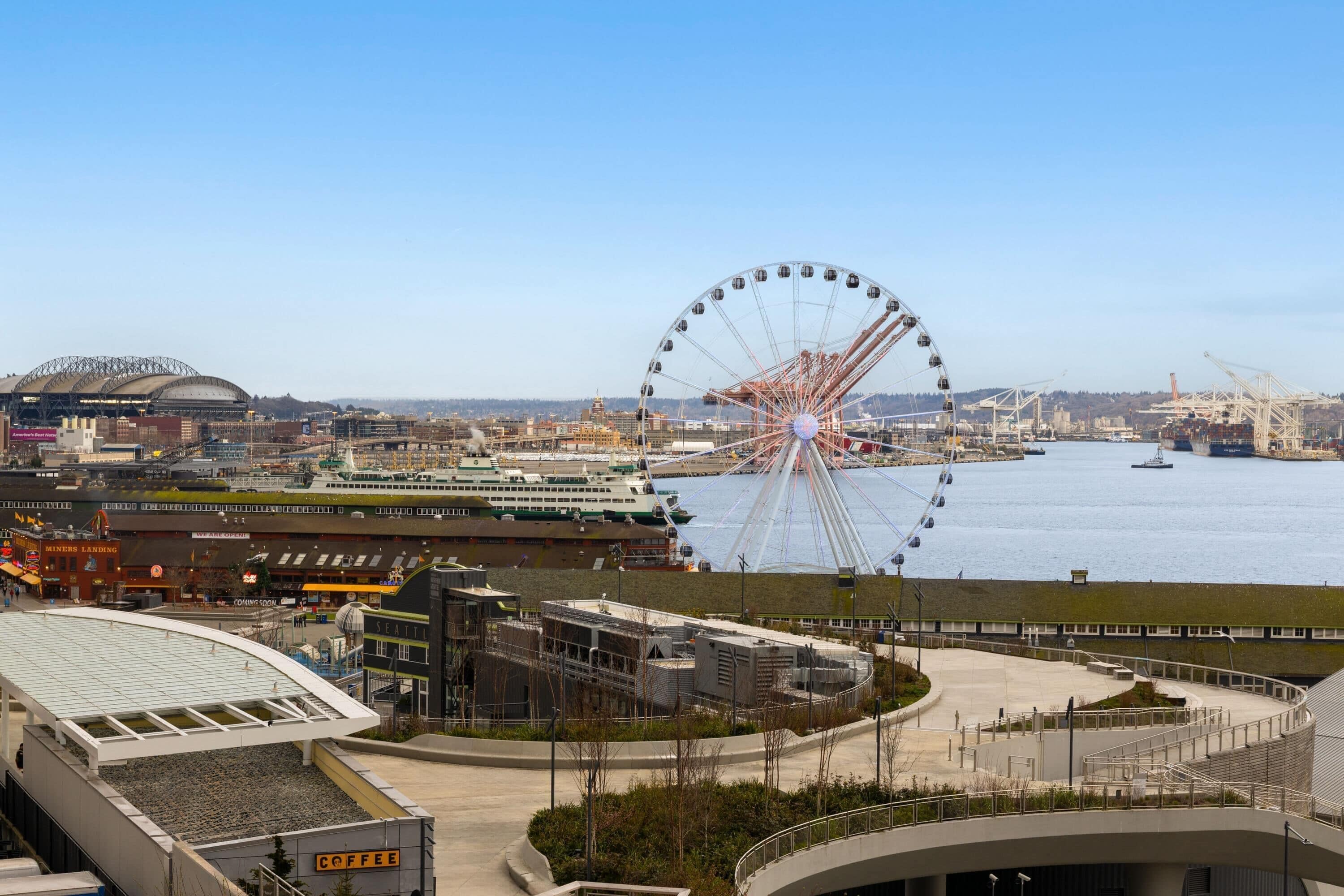 A waterfront view with a Ferris wheel, a cruise ship docked, and a modern building with a curved roof.