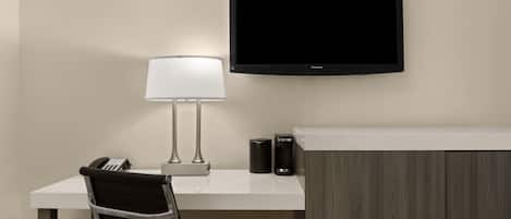 Et hotelværelse med skrivebord, stol, lampe, fladskærms-tv, telefon og skab.