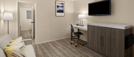 Habitación de hotel con sofá, escritorio y silla, televisor montado en la pared y puerta que da a otra habitación.