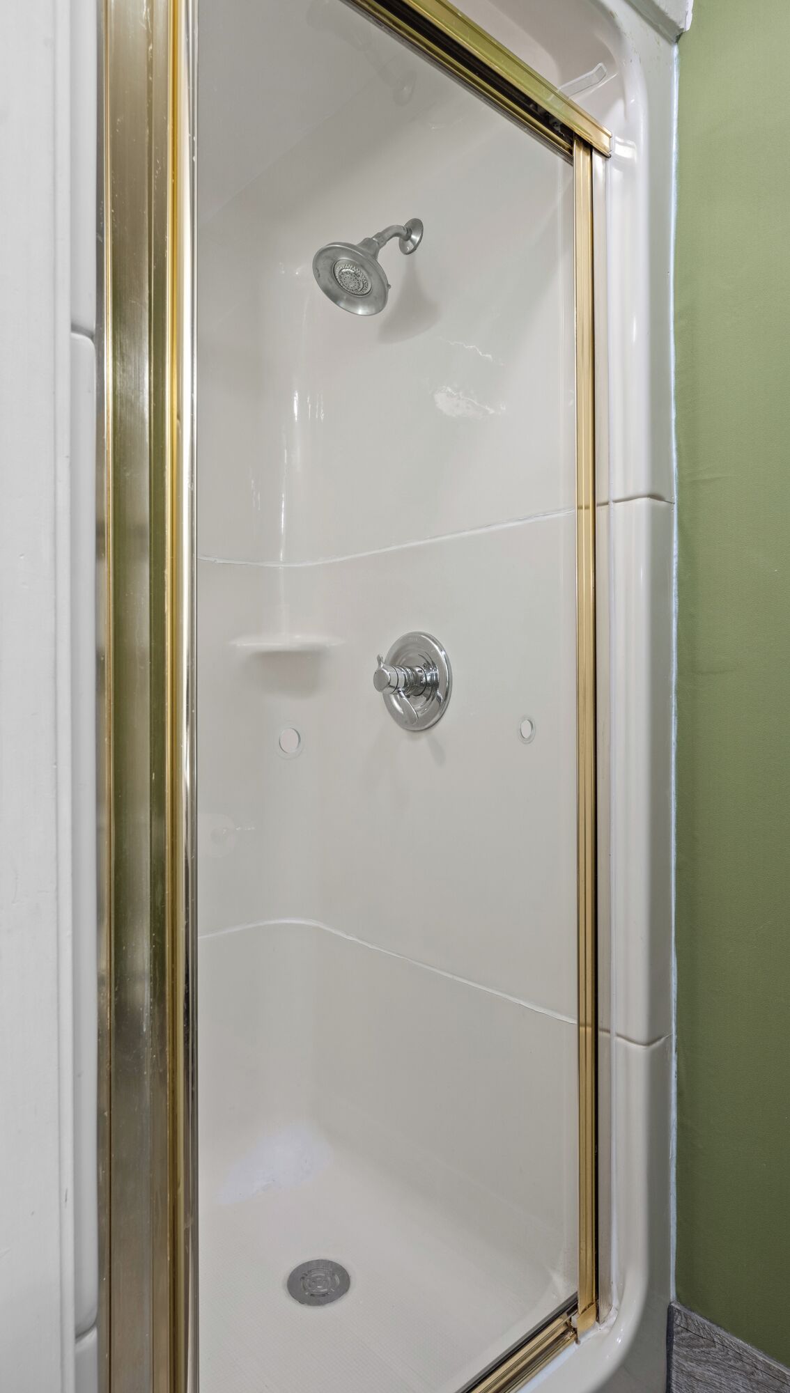A white shower enclosure with a gold frame, a showerhead, and a control knob.