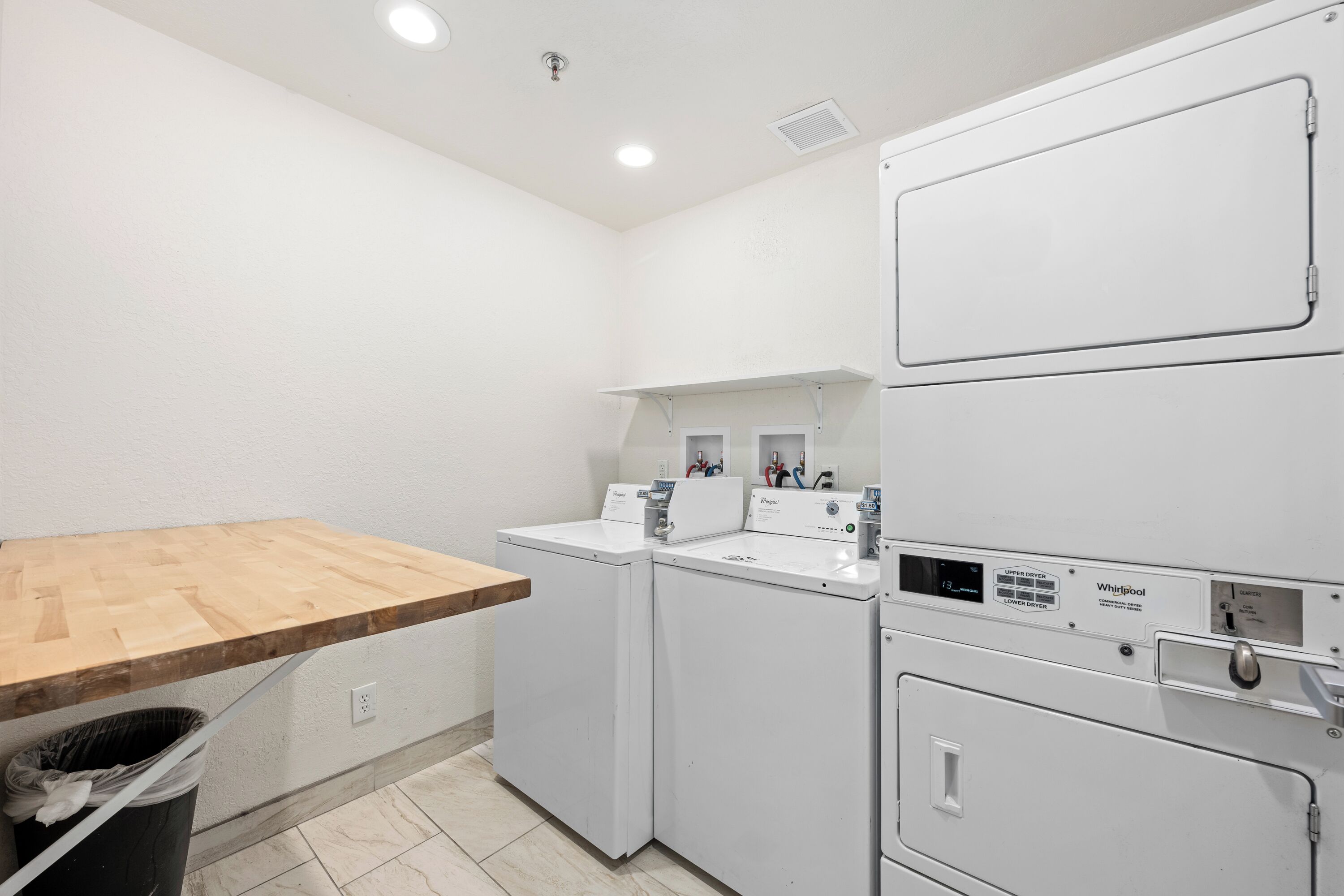 A laundry room with two washing machines, a drying rack, and a wooden table.