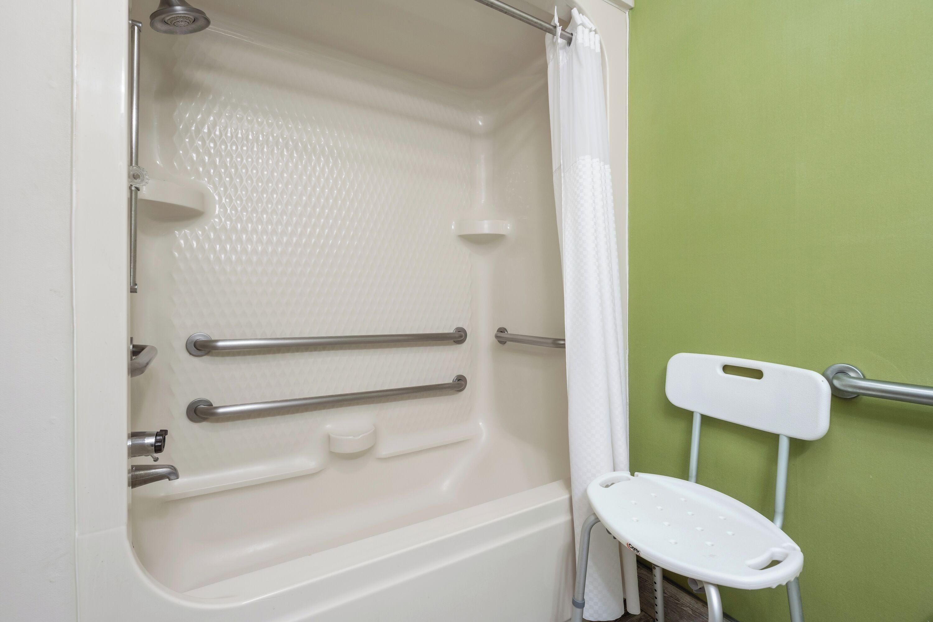 Eine Badewanne mit Handläufen, einer Duschbrause und einem weißen Stuhl.