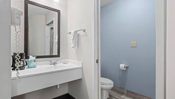 Une salle de bain avec un lavabo blanc, un miroir, un porte-serviettes, des toilettes et un sèche-cheveux.