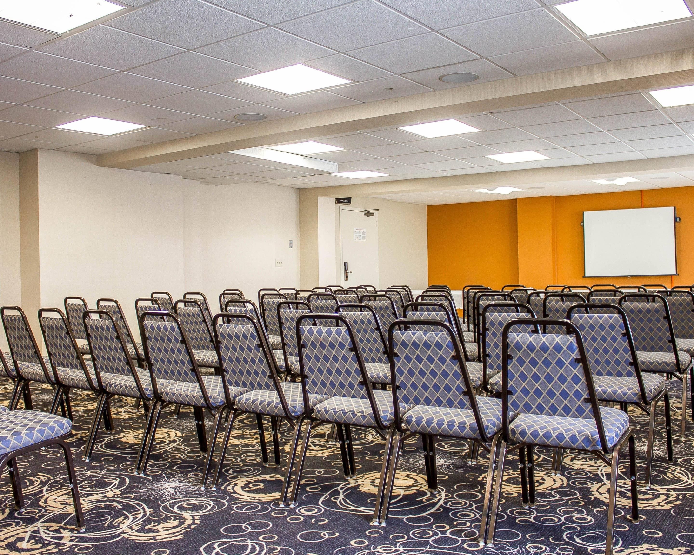 Un salón de conferencias con filas de sillas, una pizarra y suelo alfombrado.
