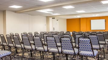 Un salón de conferencias con filas de sillas, una pizarra y suelo alfombrado.