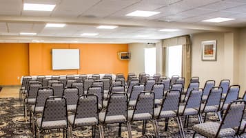 Uma sala de conferências com fileiras de cadeiras, um quadro branco e piso coberto de carpete.