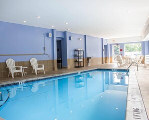 Una piscina con sillas y mesas, suelo de baldosas y pared azul.