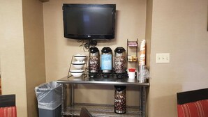 A hotel room with a flat-screen TV mounted on the wall, a coffee station with multiple coffee makers, and a trash bin. - Comfort Inn Wethersfield - Hartford (Wethersfield)