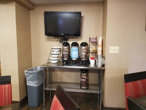 A hotel room with a flat-screen TV mounted on the wall, a coffee station with multiple coffee makers, and a trash bin. - Comfort Inn Wethersfield - Hartford (Wethersfield)