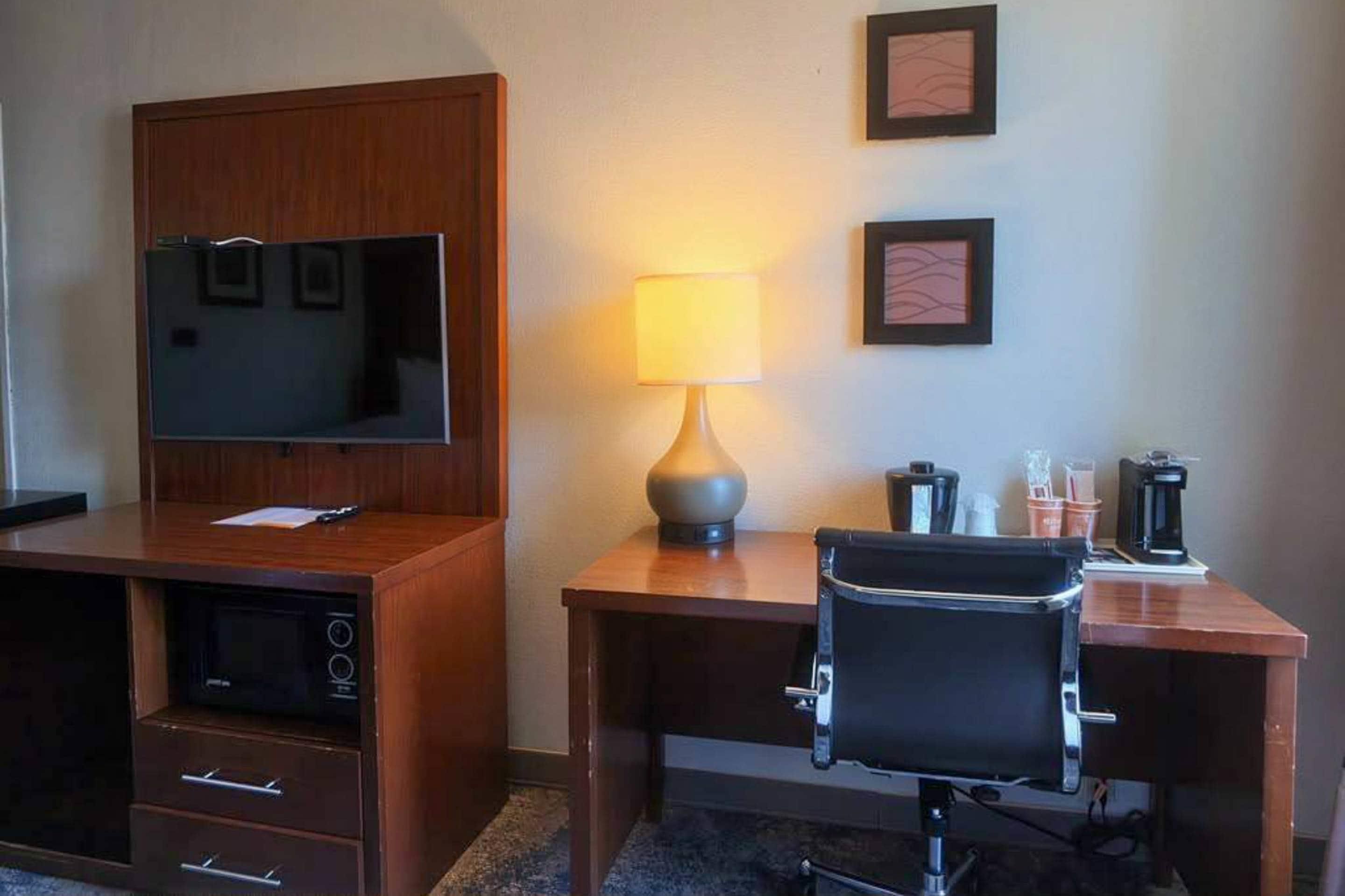 Una habitación de hotel con un escritorio de madera, una silla, un televisor, una lámpara y una cafetera.