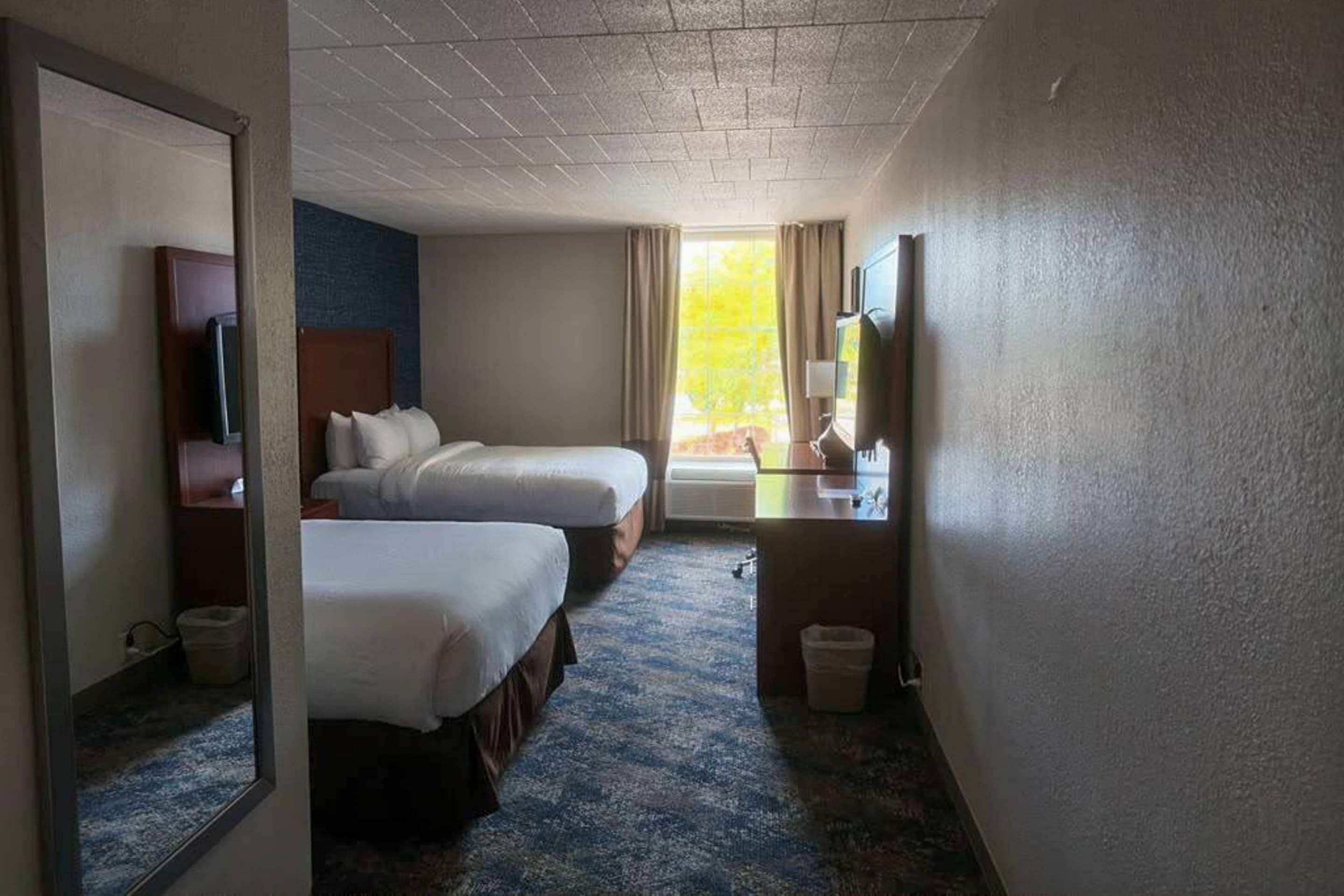 A hotel room with two beds, a desk with a chair, a television, and a window with curtains.
