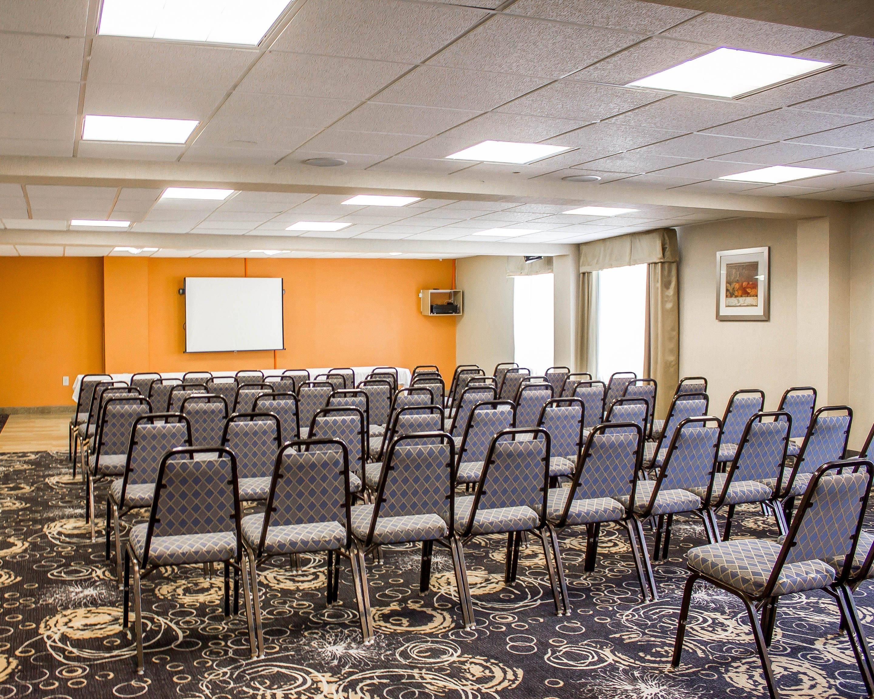 Une salle de conférence avec des rangées de chaises, un tableau blanc et un sol recouvert de moquette.