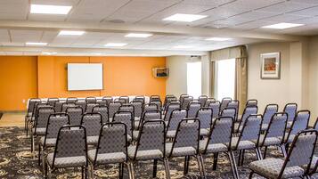 Une salle de conférence avec des rangées de chaises, un tableau blanc et un sol recouvert de moquette.
