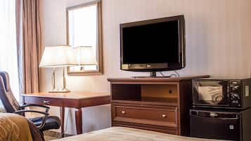 Hotellihuone, jossa on sänky, työpöytä lampun kanssa, televisio, mikroaaltouuni ja tuoli.