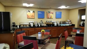 A breakfast area with tables and chairs, a coffee station, and wall posters advertising breakfast options. - Comfort Inn Wethersfield - Hartford (Wethersfield)