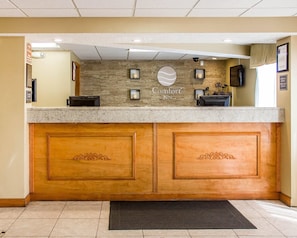 A reception desk with a stone wall backdrop, a sign reading 'Comfort Inn,' and a check-in/out schedule on the wall.