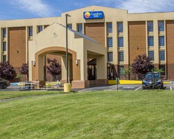 Um hotel Comfort Inn com fachada de tijolos, entrada central com arco e estacionamento com alguns carros.