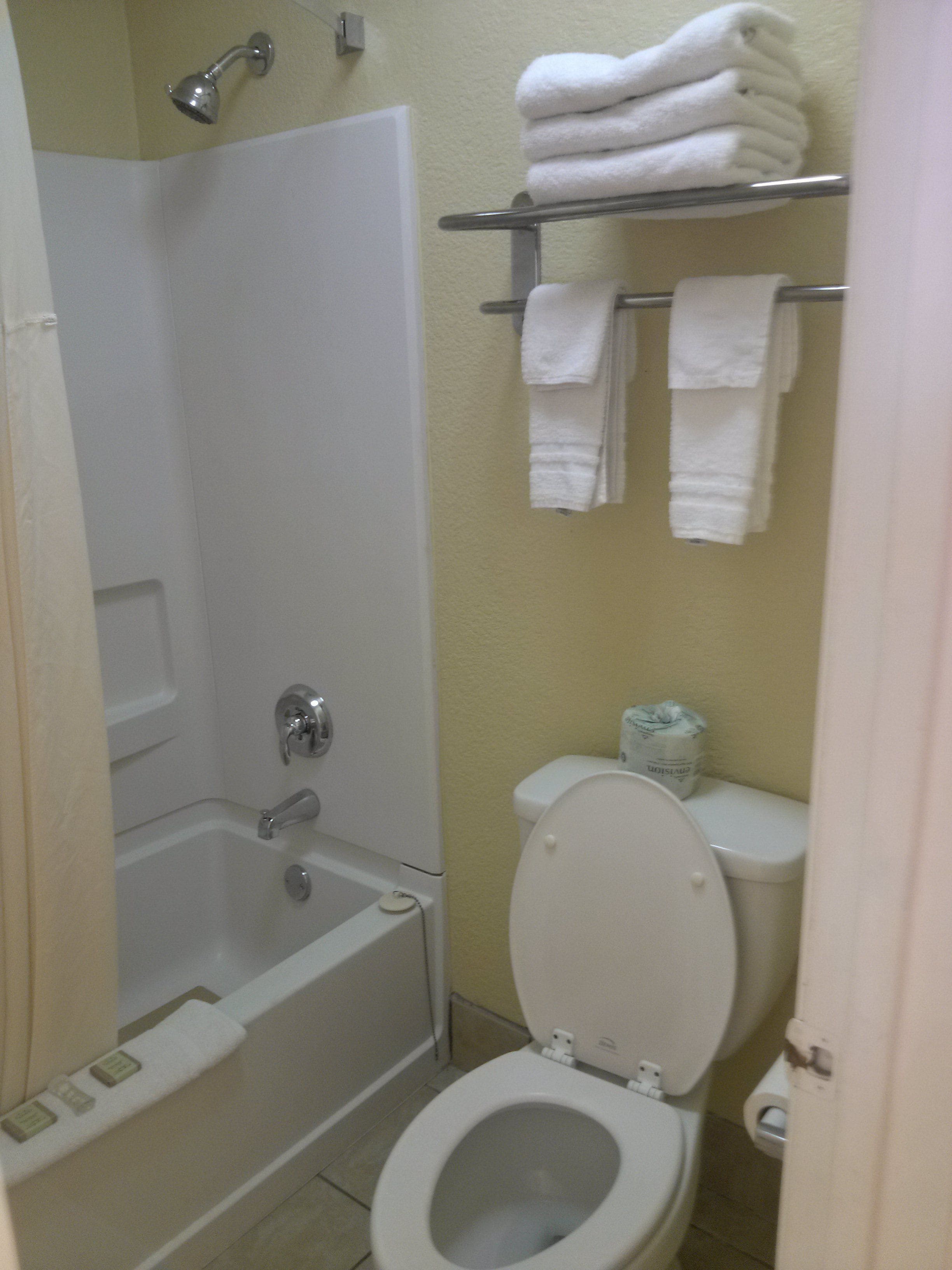 Et badeværelse med badekar, toilet og en hylde med sammenfoldede håndklæder.