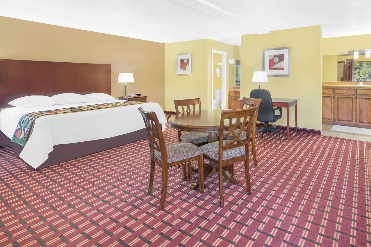 A hotel room with a bed, a dining table with chairs, a small kitchen area, and a bathroom visible through an open door.