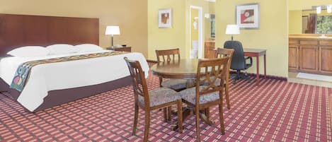 Habitación de hotel con cama, una mesa de comedor con sillas, una pequeña cocina y un baño visible a través de una puerta abierta.