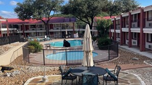 A pool area with a stone patio, lounge chairs, and umbrellas. - Super 8 by Wyndham Kerrville TX (Kerrville)