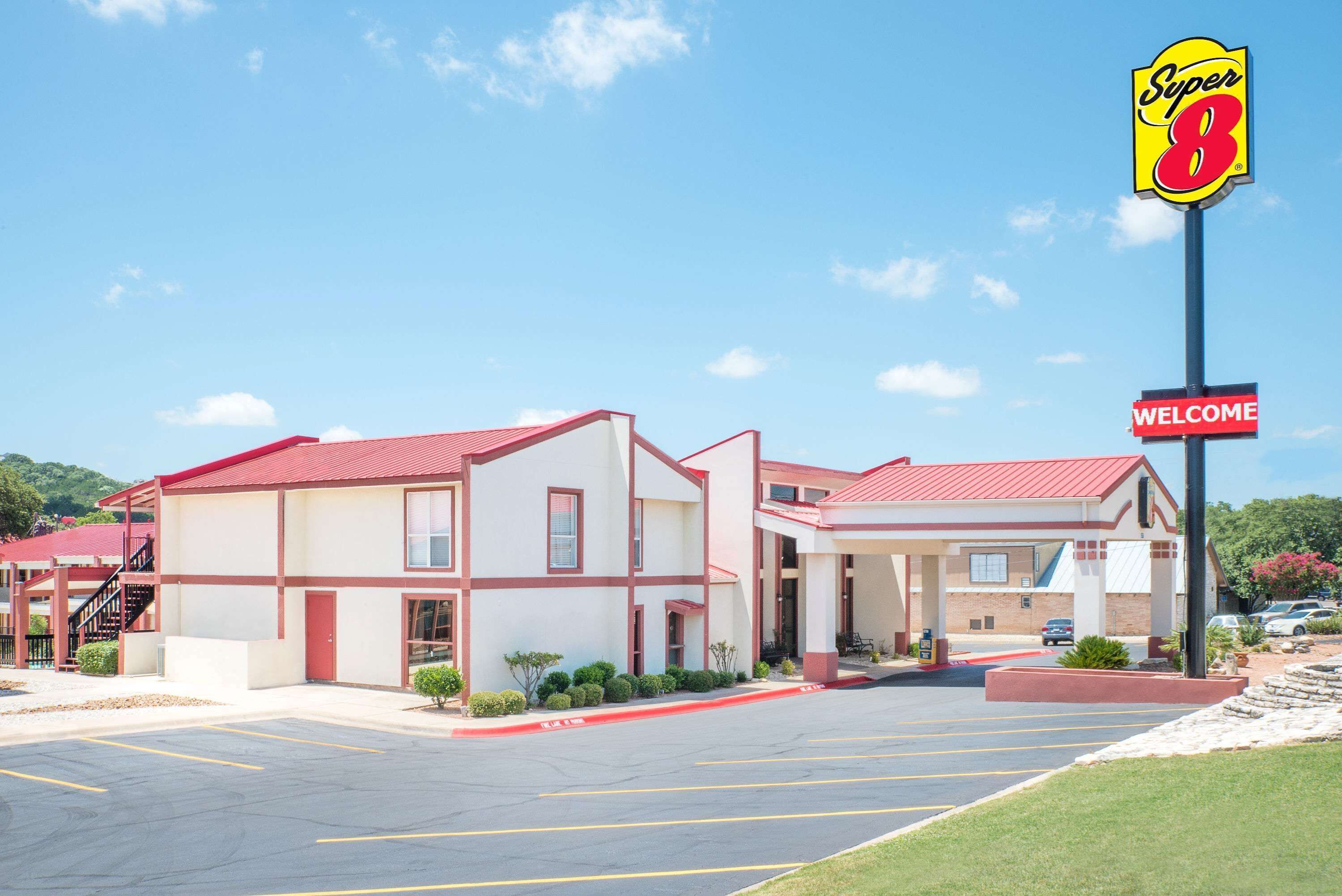 A Super 8 motel with a red roof, a welcome sign, and a parking lot.