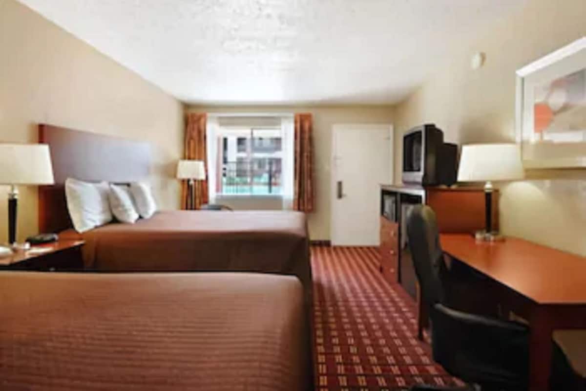 A hotel room with two beds, a desk, a chair, a television, and a window with curtains.