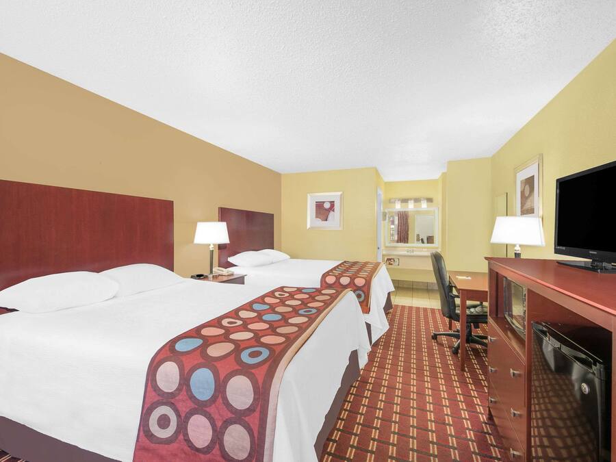 Ein Hotelzimmer mit zwei Betten, einem Schreibtisch, einem Fernseher und einem Badezimmer im Hintergrund.