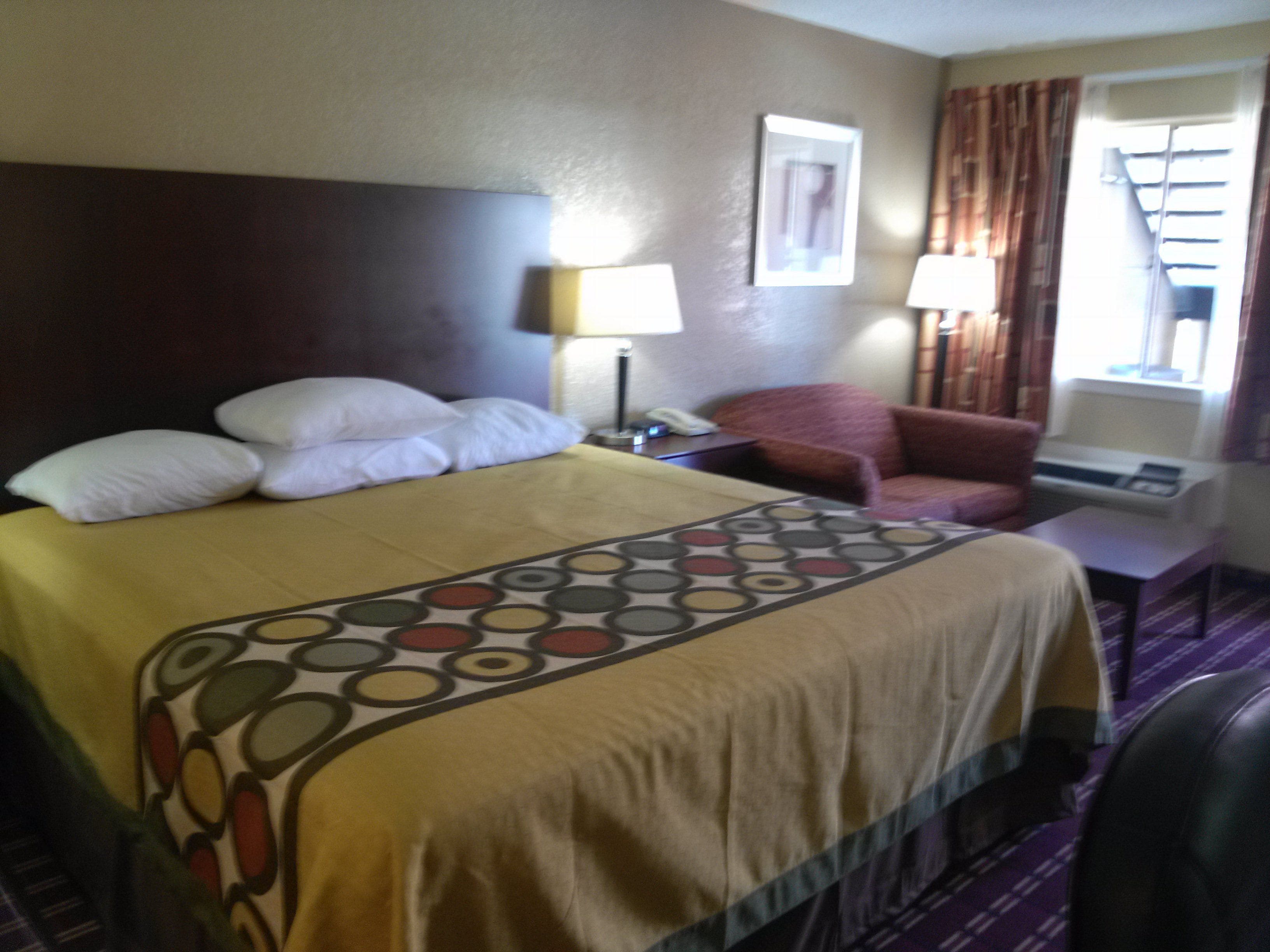A hotel room with a bed, a chair, a desk, a lamp, and a window with curtains.