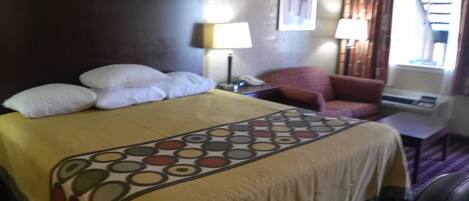 A hotel room with a bed, a chair, a desk, a lamp, and a window with curtains.