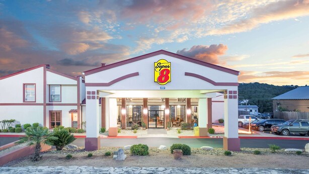 A Super 8 hotel with a modern facade, large glass entrance, and a parking lot visible in the background. - Super 8 by Wyndham Kerrville TX (Kerrville)