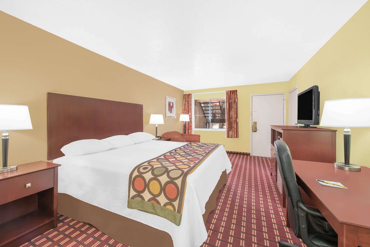 A hotel room with a bed, two bedside tables, a desk with a chair, a television, and a window with curtains.