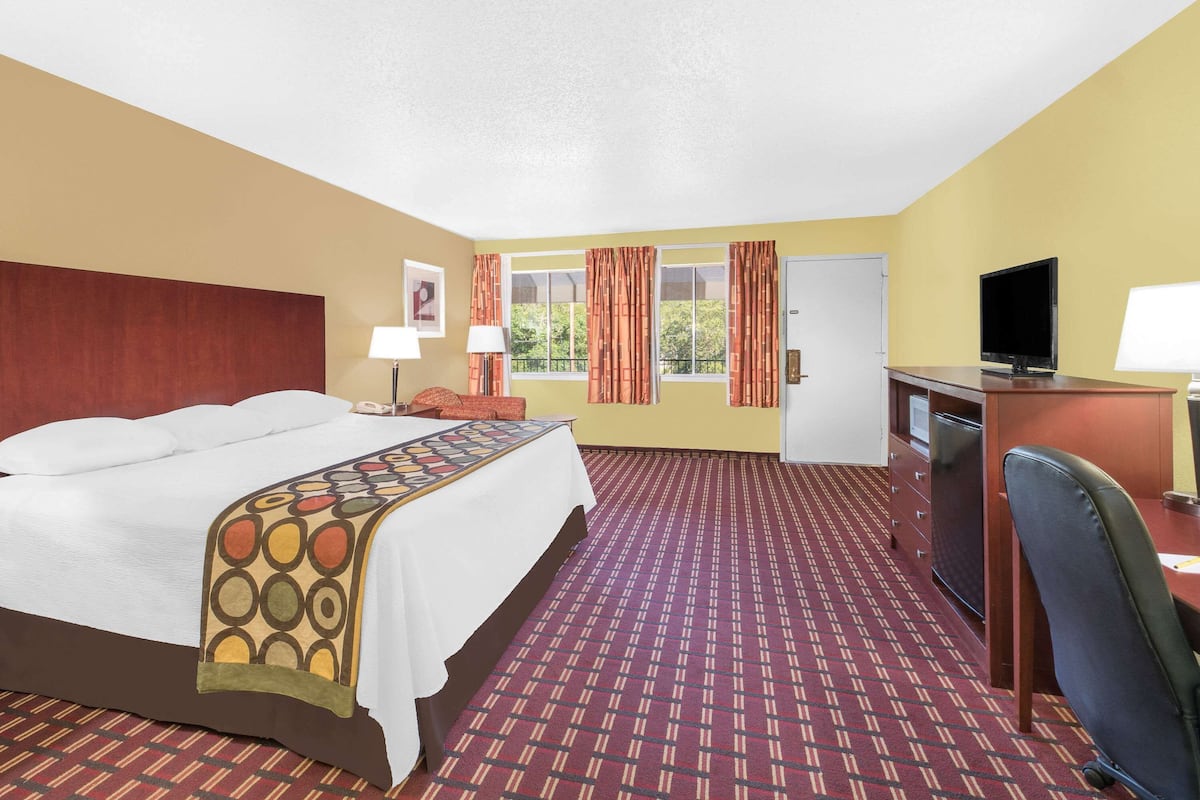 A hotel room with a bed, desk, TV, and a window with curtains.