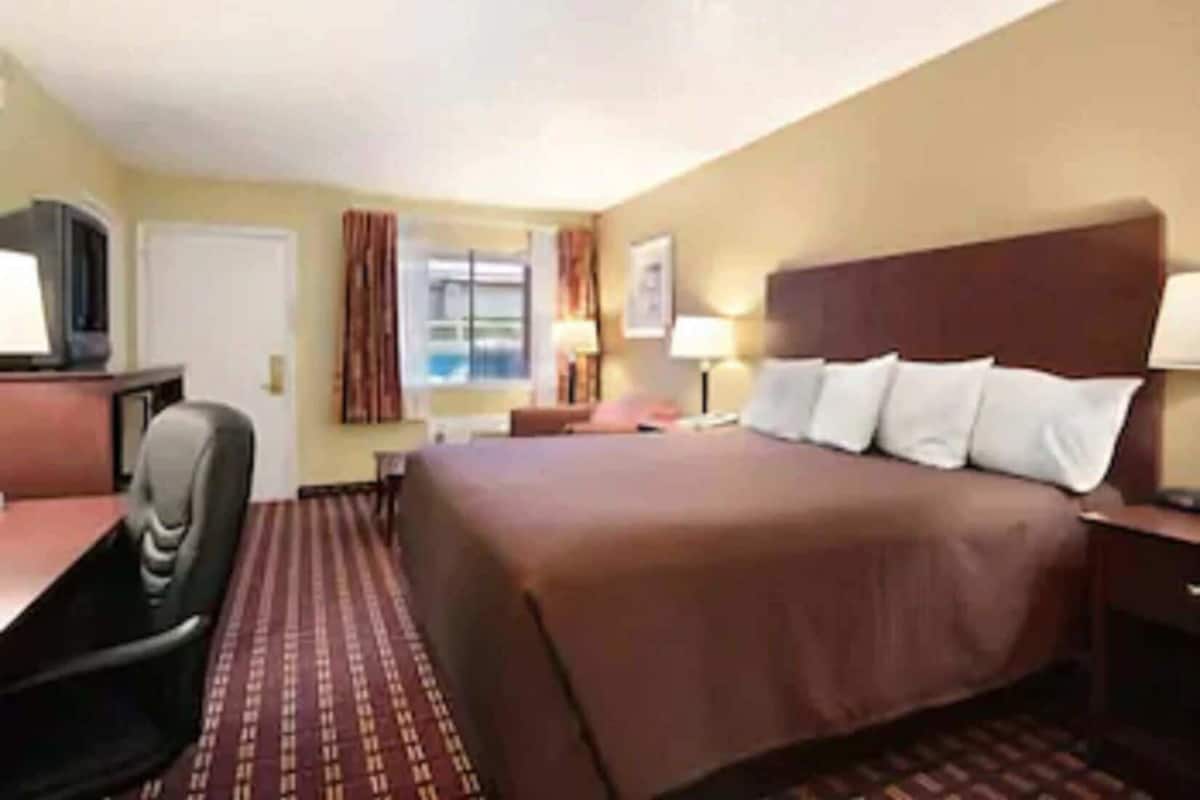 A hotel room with a bed, a desk, a chair, a television, and a window.