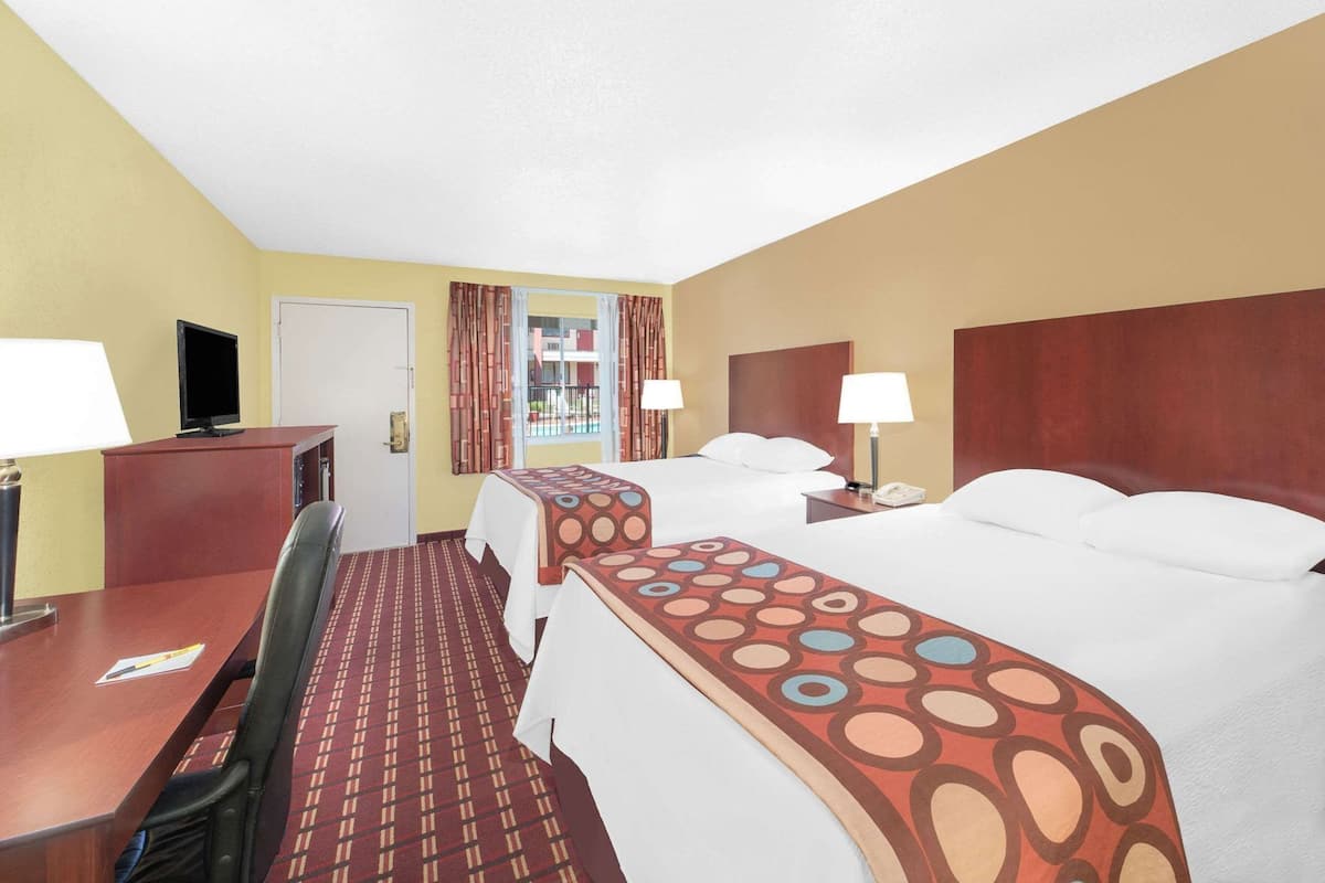 A hotel room with a desk, two beds, a TV, and a window with curtains.