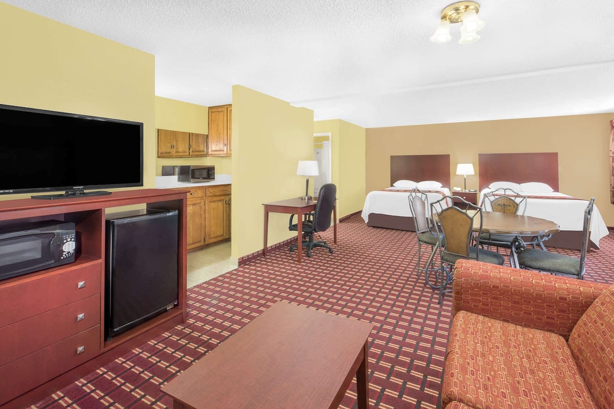 A hotel room with a television, refrigerator, microwave, desk, chair, bed, and a small dining table.