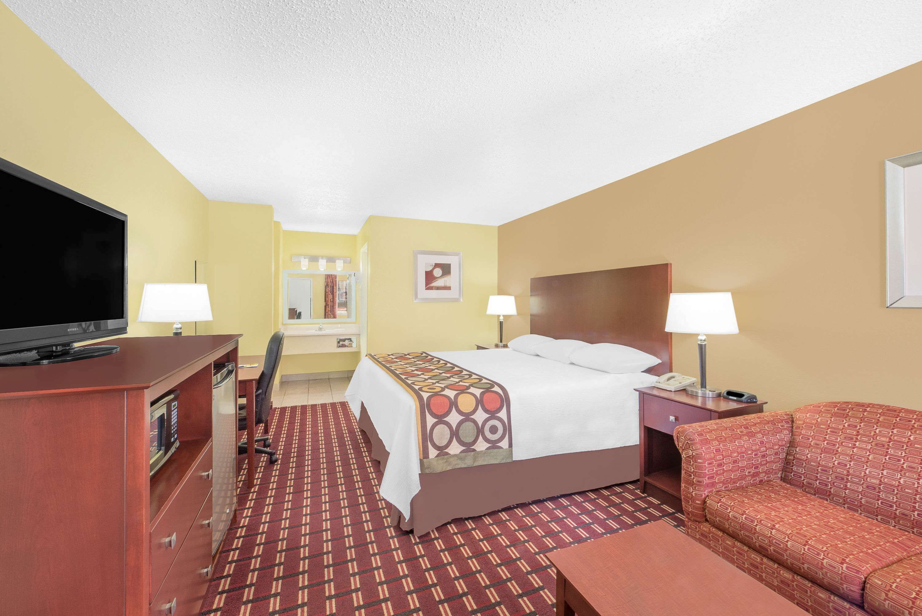 Een hotelkamer met een bed, televisie, bureau, stoel, bank en een kamerbreed tapijt met patroon.
