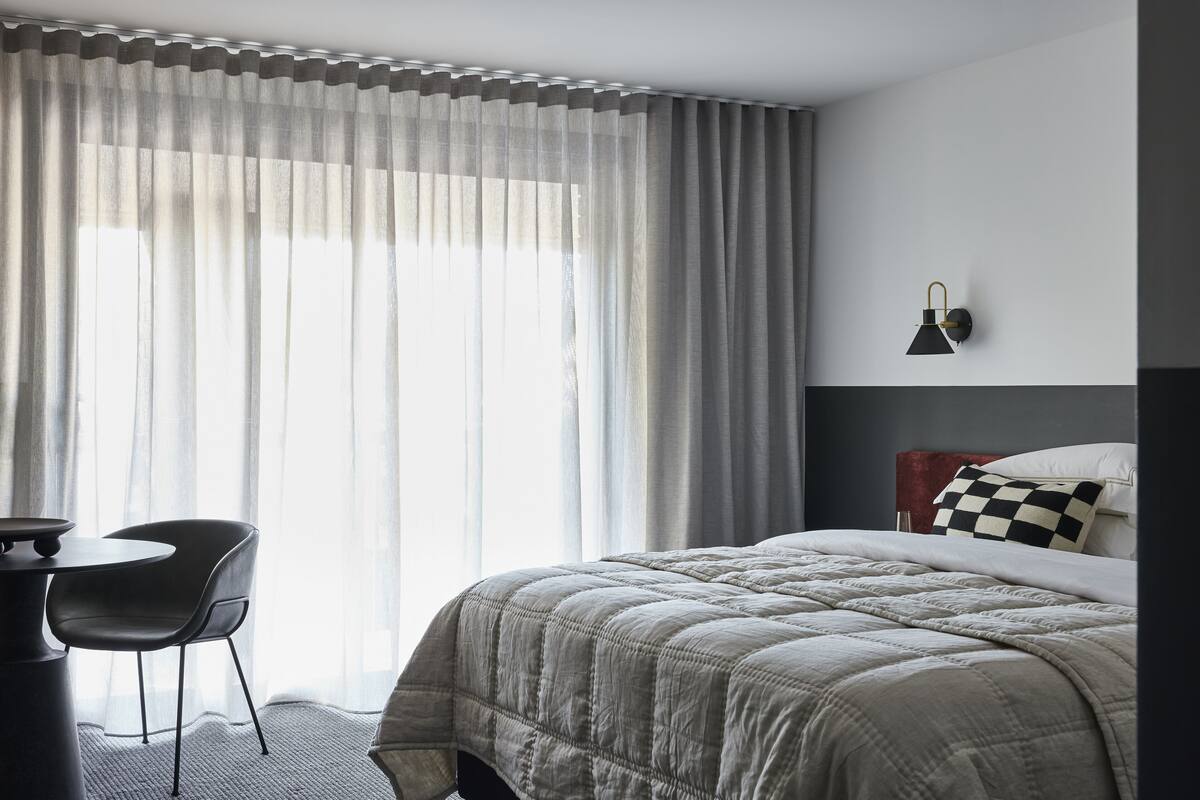 A hotel room with a bed, a desk, a chair, and a window with curtains.