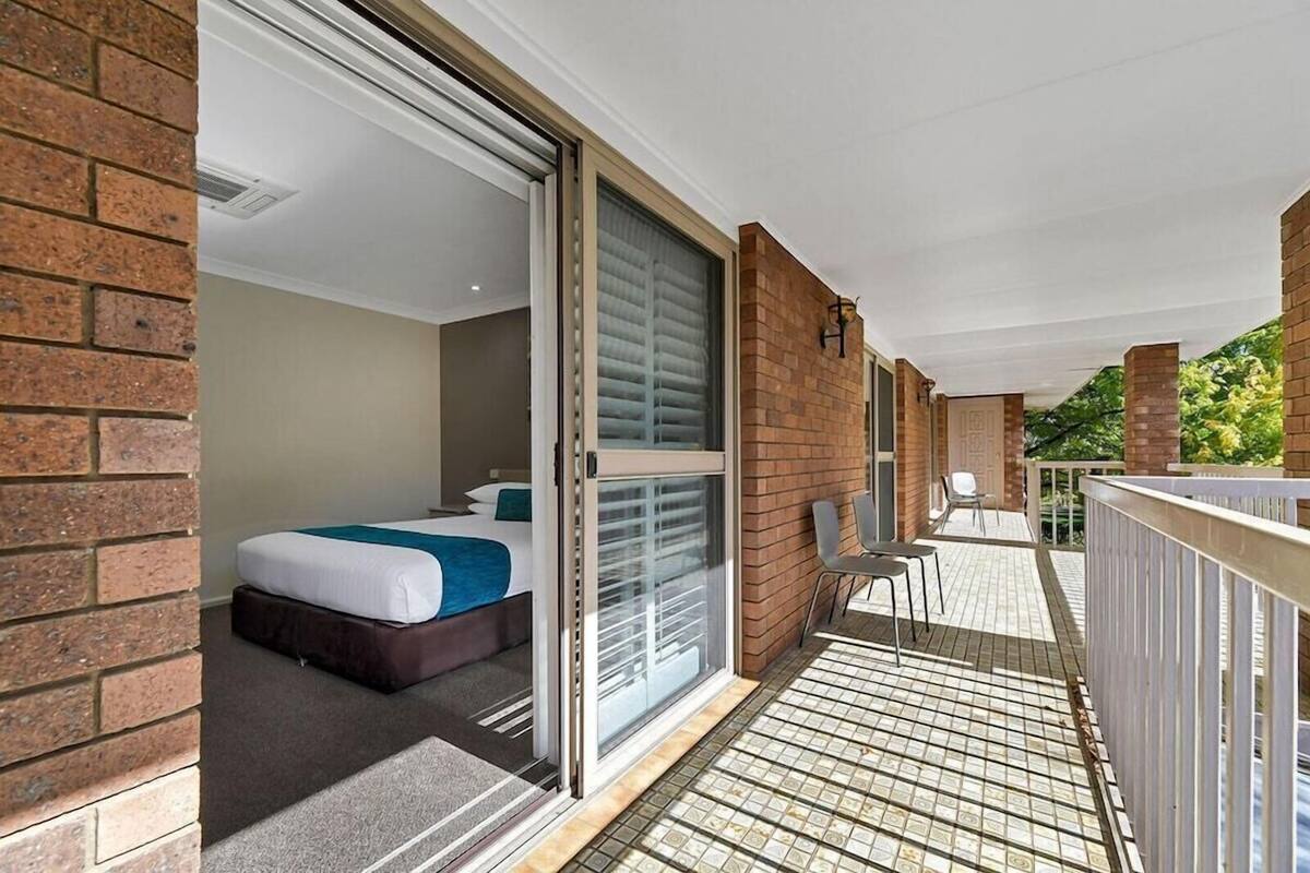 A hotel room with a bed, a sliding glass door to a balcony, and a small outdoor seating area.