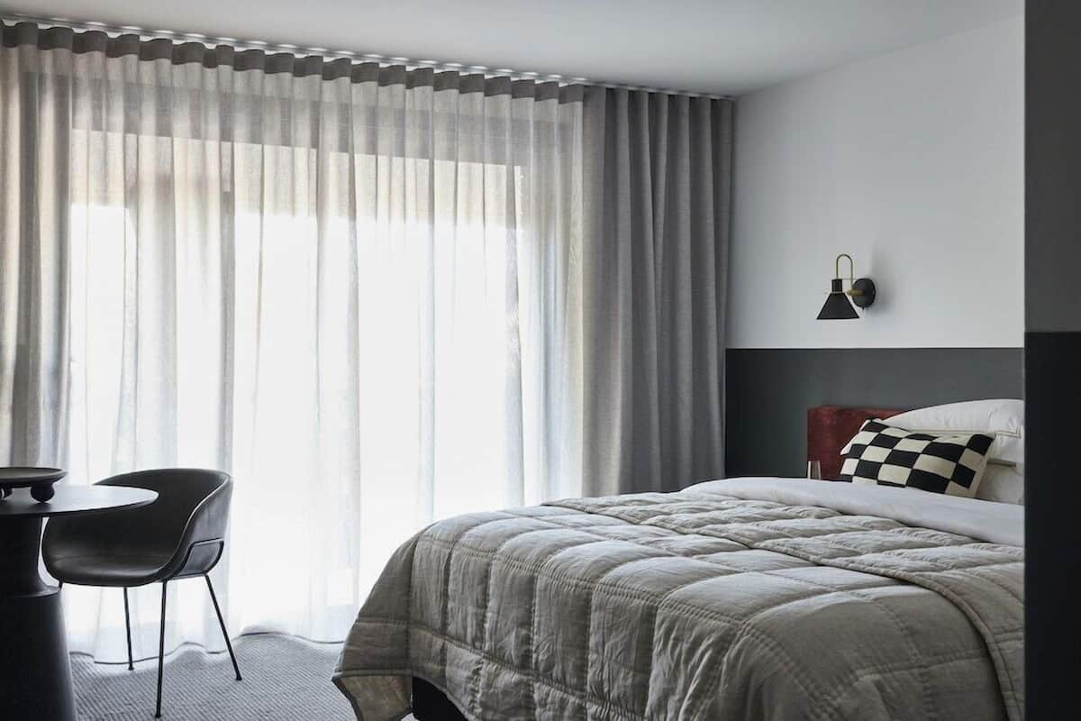 A modern hotel room with a large bed, a desk, and a chair.