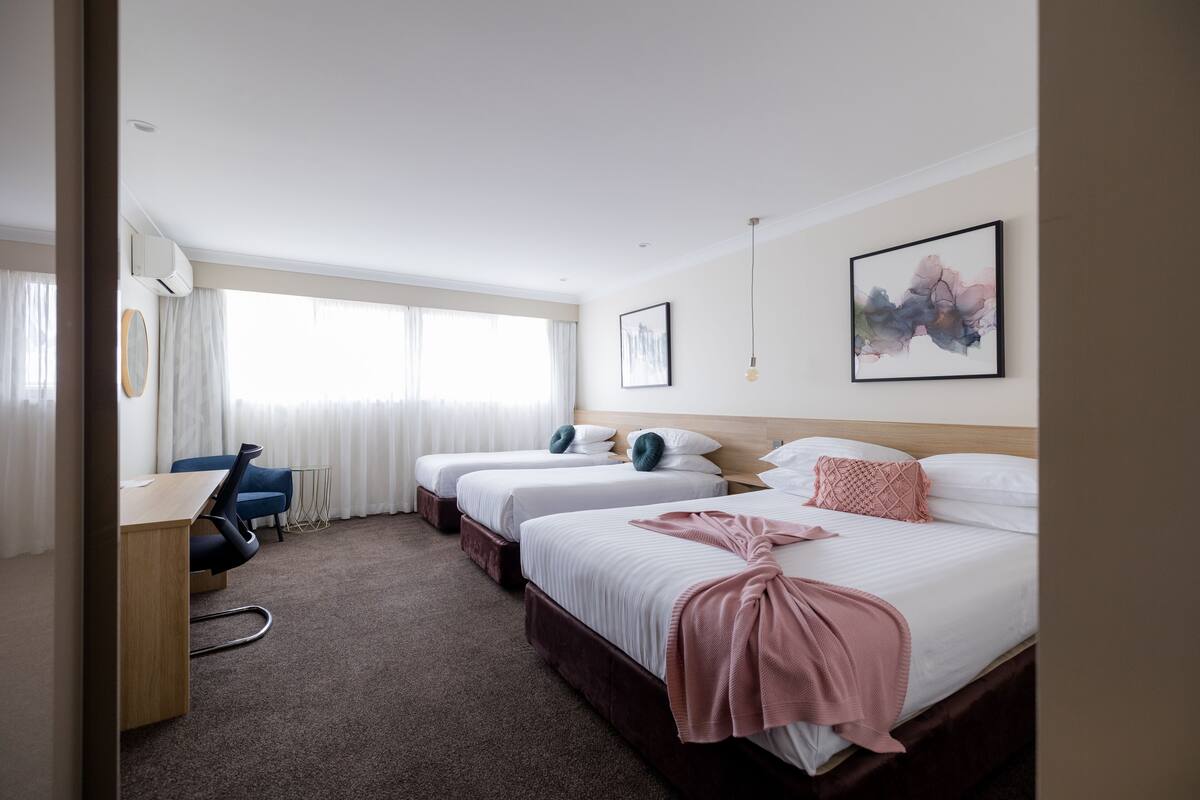 A hotel room with three beds, a desk, and a chair.
