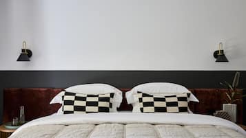 Una cama impecable con un cojín de cuadros, cabecero oscuro y dos lámparas de pared.