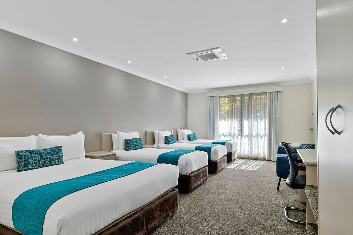 A hotel room with three beds, a desk, and a chair.