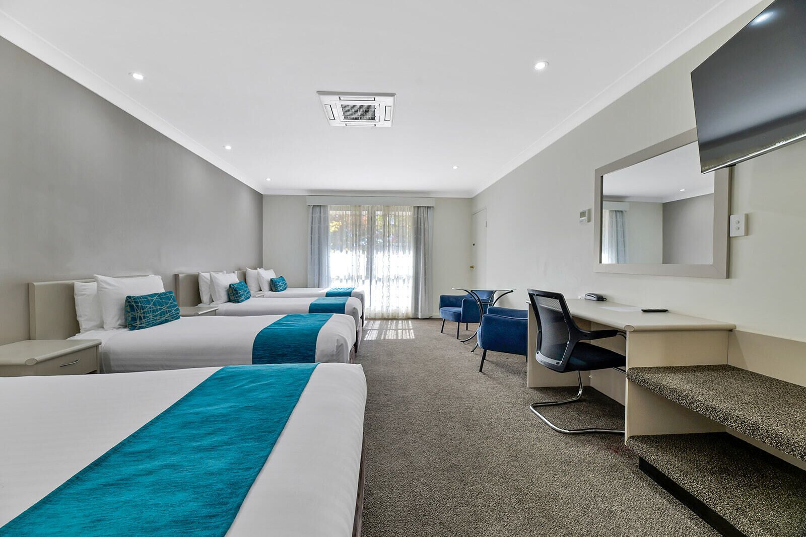 A hotel room with two beds, a desk, a chair, and a large mirror.