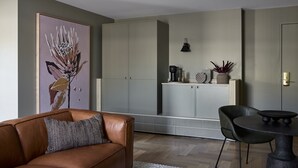 A modern living room with a brown leather sofa, a dining table with two chairs, a kitchen area with cabinets, and a large abstract painting on the wall. - Central Caleula Motor Lodge (Orange)