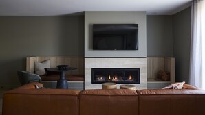A modern living room with a fireplace, a flat-screen TV mounted above it, and a comfortable seating area with a sofa and a chair. - Central Caleula Motor Lodge (Orange)