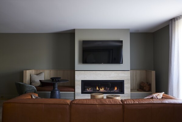 A modern living room with a fireplace, a flat-screen TV mounted above it, and a comfortable seating area with a sofa and a chair.