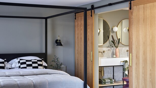 A modern bedroom with a large bed, a wooden wardrobe, and a bathroom visible through an open door. - Central Caleula Motor Lodge (Orange)