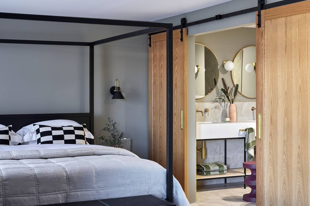 A modern bedroom with a large bed, a wooden wardrobe, and a bathroom visible through an open door.